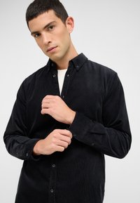 Schwarzes Cordhemd mit Knopfleistenkragen, langen Ärmeln und strukturierter Oberfläche. Verfügt über vordere Knöpfe und verstellbare Manschetten.