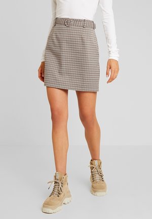 Jupe mini à carreaux marron avec une ceinture, taille haute, et deux poches latérales, associée à des bottes beiges à lacets et un haut ajusté à manches longues blanc.