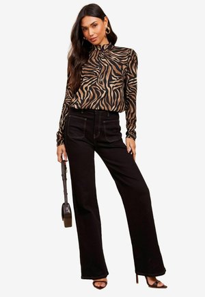 Maglietta a maniche lunghe con motivo a strisce zebra nera e beige; abbinata a jeans a vita alta neri con gamba larga e sandali neri con punta aperta.