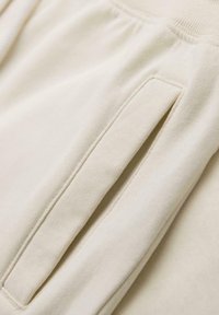 Gros plan sur un pantalon de jogging en tissu beige, montrant une poche latérale avec des coutures visibles et une ceinture élastique.