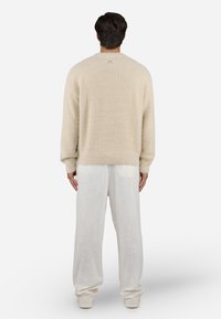 Cream-colored sweater made of soft, textured fabric with a relaxed fit. Paired with loose, light-colored linen trousers.