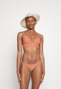 Bikini set v ružovej farbe s trojuholníkovým vrchom s úzkymi popruhmi a textúrovaným povrchom, doplnený zodpovedajúcimi nízkymi spodkami.