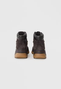 Footwear featuring a high-top design made of dark gray suede with black leather accents and a tan rubber sole. No visible laces.