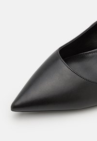 Black leather pointed toe shoe with a smooth texture, low-cut design, and minimal stitching details along the edges.