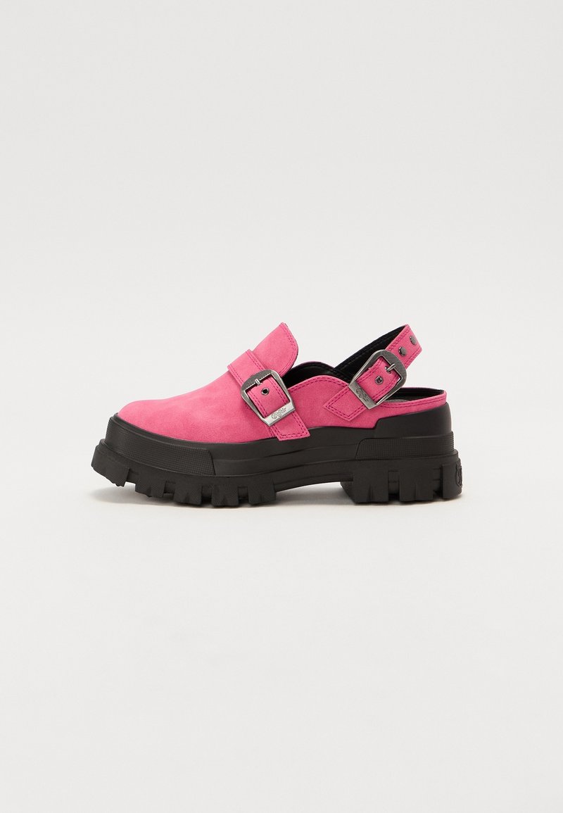 Sabot en suède rose avec semelle épaisse en caoutchouc noir, boucles argentées réglables sur la bride et le talon, et design arrière ouvert.