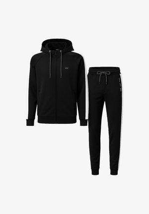Chándal negro que incluye una sudadera con capucha y cremallera con franjas laterales blancas y pantalones a juego con cintura con cordón. Fabricado en material suave y elástico.