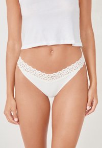 Weiße Tanga-Unterwäsche mit einem zarten Spitzenbesatz entlang des Bundes, glattem Stoff und einer dreieckigen Form, die minimalen Schutz bietet.
