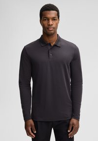 Koszulka polo z długim rękawem w ciemnoszarej bawełnie. Posiada klasyczny kołnierzyk, rozporki na trzy guziki oraz subtelne detale przeszyć.