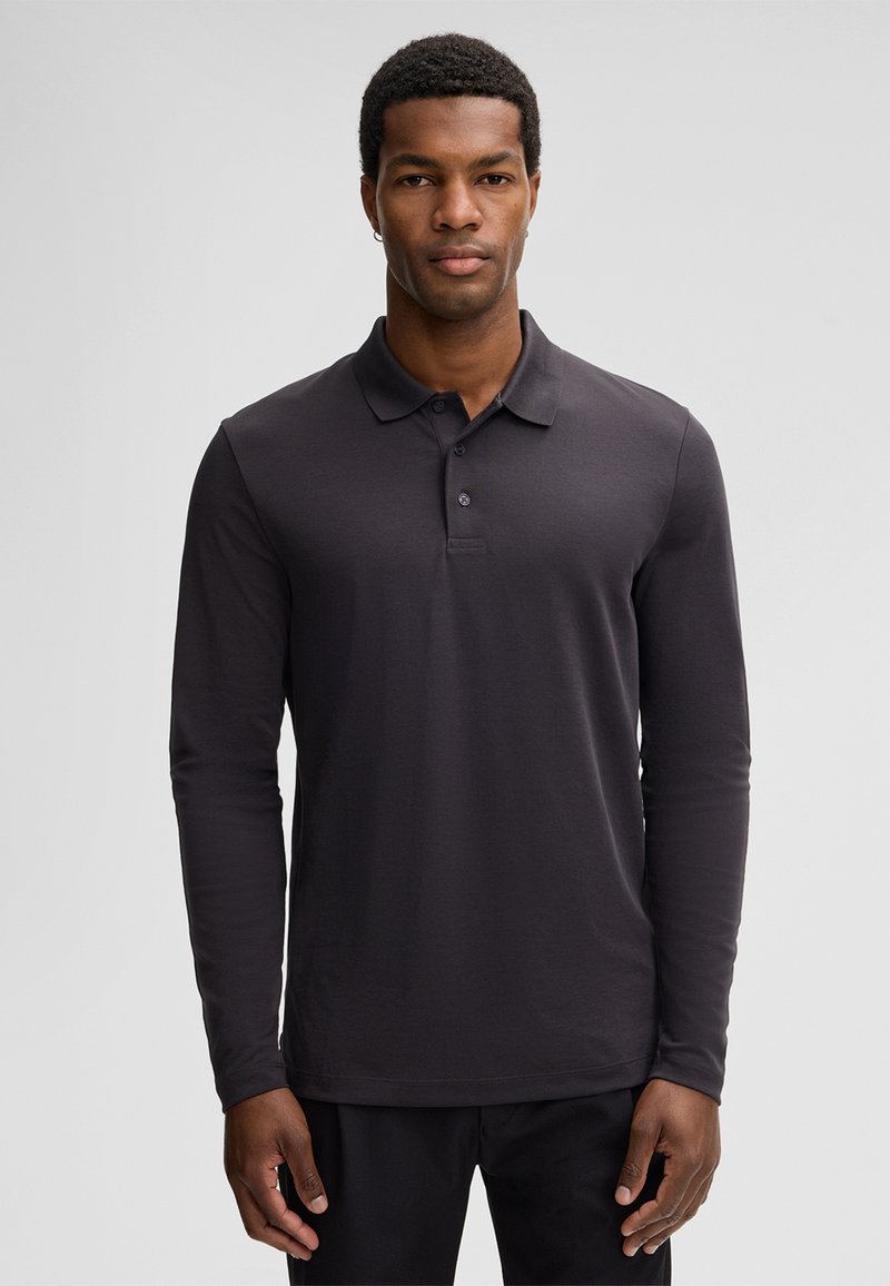 Koszulka polo z długim rękawem w ciemnoszarej bawełnie. Posiada klasyczny kołnierzyk, rozporki na trzy guziki oraz subtelne detale przeszyć.