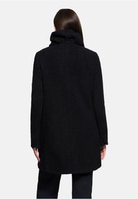 Zwarte jas met een gestructureerd oppervlak, hoge kraag en lange mouwen. Beperkte zichtbare details op de achterkant. Eenvoudig, recht gesneden ontwerp.