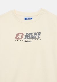 Béžové bavlnené tričko s grafickou potlačou "JACK & JONES" v farebných písmenách a zaobleným výstrihom. Mäkký povrch.