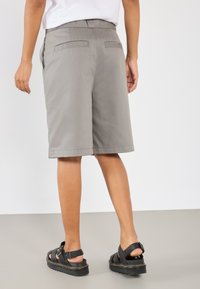 Gray knee-length shorts with a smooth texture, featuring two back pockets. Paired with black sandals with a chunky sole and adjustable straps.
