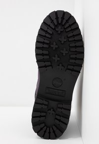 Suela de goma negra de una bota, con un patrón de tracción rugoso y el logo de Timberland grabado en el lateral.