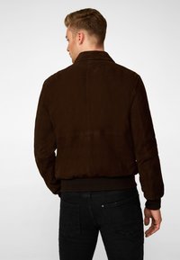 Brown suede jacket with a ribbed hem and collar, featuring a smooth texture and minimalist design, worn with dark jeans.