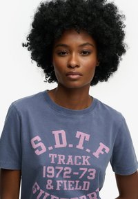 Donkerblauw katoenen T-shirt met opvallende, roze grafische tekst. Ronde halslijn en korte mouwen met een casual pasvorm. Eenvoudig ontwerp.