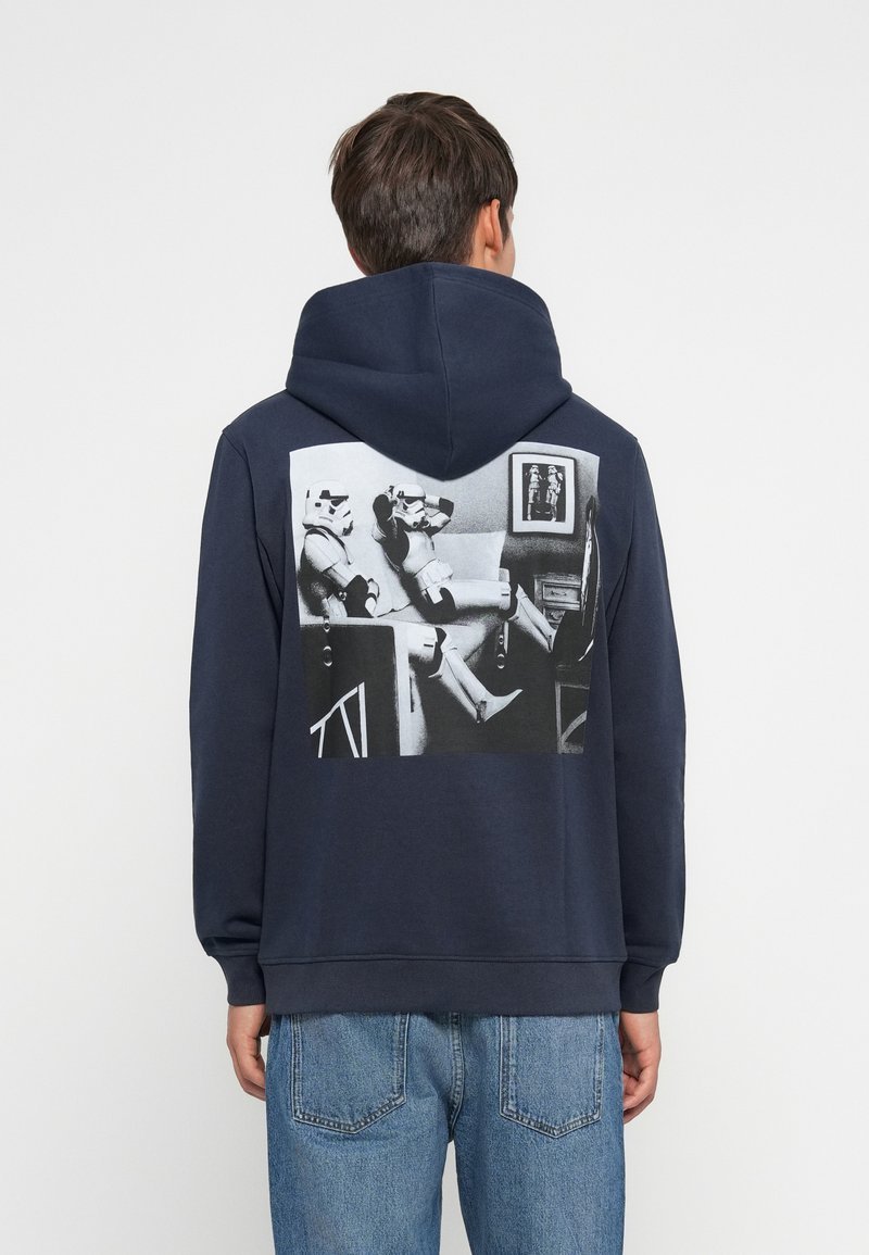 Granatowy hoodie z dużą czarno-białą grafiką na plecach, przedstawiającą dwóch szturmowców siedzących. Miękka tkanina, luźny krój i kieszeń kangurzą.