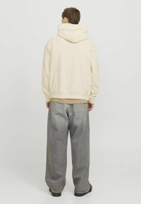 Bež hoodie s velikom kapuljačom, teksturiranom tkaninom, rebrastim manžetama i rubom; uparen s labavim, izblijeđenim sivim trapericama i crnim cipelama.