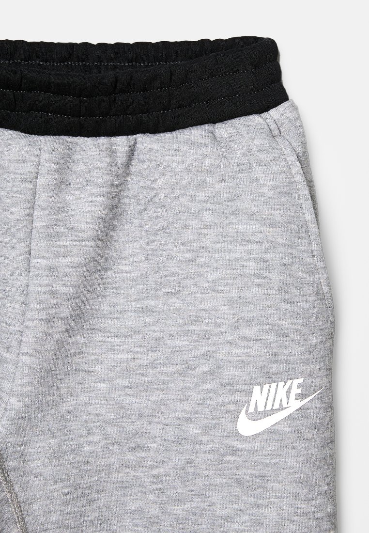 Grijze sweatpants met een zwarte elastische tailleband en een wit "Nike" logo op de linkeronderzijde. Zachte textuur met een gemêleerd uiterlijk.