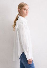 Witte longsleeve shirt van katoen, met een traditionele kraag, verlaagde schouders en een gebogen zoom. Gecombineerd met blauwe jeans.