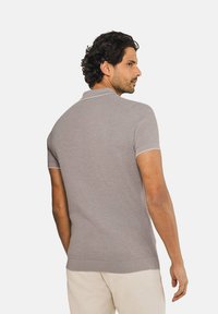 Lichtgrijs poloshirt met korte mouwen, voorzien van een gestructureerd patroon, contrasterende kraag en afgewerkte manchetten. De stof lijkt soepel en aansluitend.