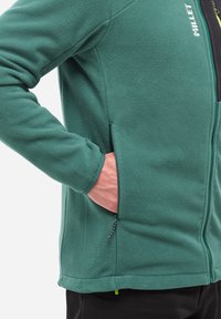 Veste en polaire verte avec une poche zippée, tissu texturé et poignets élastiques. Présente une fermeture zippée et un design ajusté.