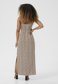 Maxi dress in a beige fabric with a black leopard print design. Features a straight back, adjustable straps, and a side slit.