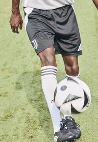 Sorte fodboldshorts med hvide striber, hvide strømper med tre sorte striber og sorte fodboldstøvler, mens en fodbold bliver sparket.