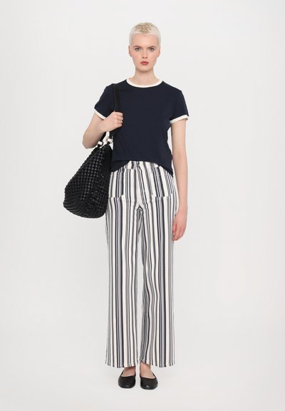 T-shirt blu navy con rifiniture crema, abbinato a pantaloni a gamba larga bianchi e blu a righe. Una borsa intrecciata nera e delle ballerine nere completano il look.