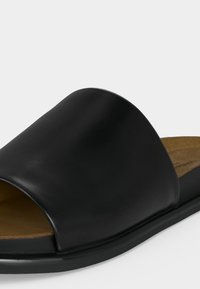 Μαύρο σανδάλι slide με ανοιχτά δάχτυλα, λείο δερμάτινο πάνω μέρος και επίπεδη σόλα σε λευκό φόντο.