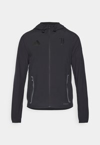 Giacca sportiva nera con cappuccio, dotata di tasche con zip, logo Adidas ed emblema della Juventus. Realizzata in tessuto leggero e testurizzato.