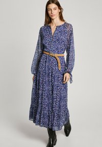 Pitkä, liian vaalean sininen mekko, jossa on kukkakuviot, nyörikuvioidut hihat, V-pääntie ja punottu vaaleanruskea vyö. Polven pituinen röyhelö helman reunassa.