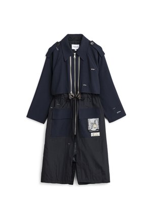 Abrigo largo azul marino con dobles cremalleras, grandes bolsillos delanteros, detalles bordados en forma de ojos, parche con diseño gráfico y charreteras en los hombros.