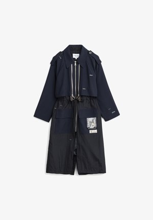 Abrigo largo azul marino con dobles cremalleras, grandes bolsillos delanteros, detalles bordados en forma de ojos, parche con diseño gráfico y charreteras en los hombros.