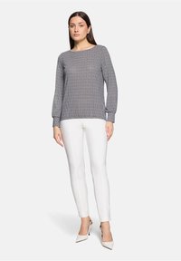 Grijze textuurtrui met lange mouwen, ronde halslijn en geribbelde boorden, gecombineerd met strakke witte broek en puntige beige hakken.