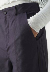 Tmavě fialové kalhoty s vertikálními proužky, obsahující boční kapsy a plochý přední díl, vyrobené z hladkého, texturovaného materiálu.