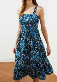 Blumenkleid mit ärmellosem Design, das einen quadratischen Ausschnitt und blau-orangefarbene Blumenmuster auf einem dunkelblauen Hintergrund zeigt.