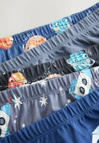 Sous-vêtements pour enfants avec ceintures élastiques présentant des motifs colorés sur le thème de l'espace, incluant des planètes, des étoiles et des fusées sur un tissu bleu et gris.
