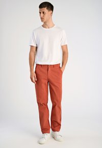 Rode katoenen broek met rechte pijpen, steekzakken aan de voorkant en een knoopsluiting, gecombineerd met een wit T-shirt met ronde hals en witte sneakers.