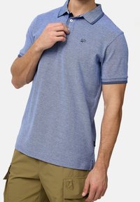 Polo bleu clair en tissu texturé, avec un col boutonné et des accents bleu marine contrastants sur les poignets et le col. Logo subtil sur la poitrine.