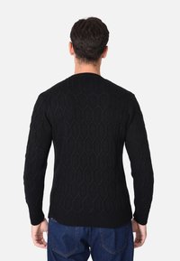 Maglione nero a maglia con un motivo esagonale testurizzato, maniche lunghe e orlo a coste. Dettagli delle cuciture visibili sulle spalle e sui polsini.