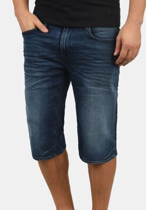 Pantalones cortos de mezclilla en un lavado azul oscuro con una textura ligeramente deslavada, de longitud hasta la rodilla, con diseño de cinco bolsillos y detalles de costura visibles.