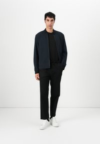 Jachetă de bomber navy, tricou negru cu guler rotund, pantaloni negri și adidași albi. Material neted, tăietură casual, design minimalist.