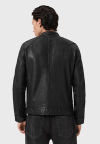 Zwarte leren jas met een aansluitend ontwerp, met een gladde textuur en gestructureerde naden, van achteren getoond, gecombineerd met donkere jeans.