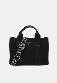 Černá plátěná kabelka s dvojitými horními rukojeťmi, nastavitelným popruhem s bílým logem a trojúhelníkovou logovou plaketou na přední straně.