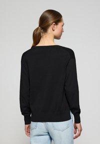 Svart, långärmad sweatshirt med rundad halsringning och ribbad mudd. Tillverkad av mjukt material, med en avslappnad passform och subtila sömdetaljer.