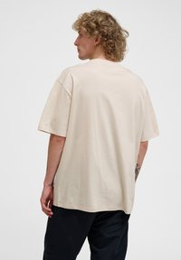 Beige oversized T-shirt lavet af bomuld, med en klassisk rund hals, korte ærmer og en glat tekstur. Bagfra uden synlige grafikker.