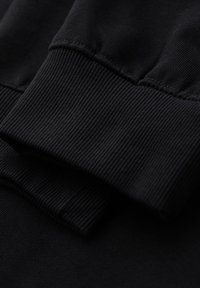 Primer plano de los puños de una sudadera negra acanalada que muestran las costuras detalladas y la textura del tejido.