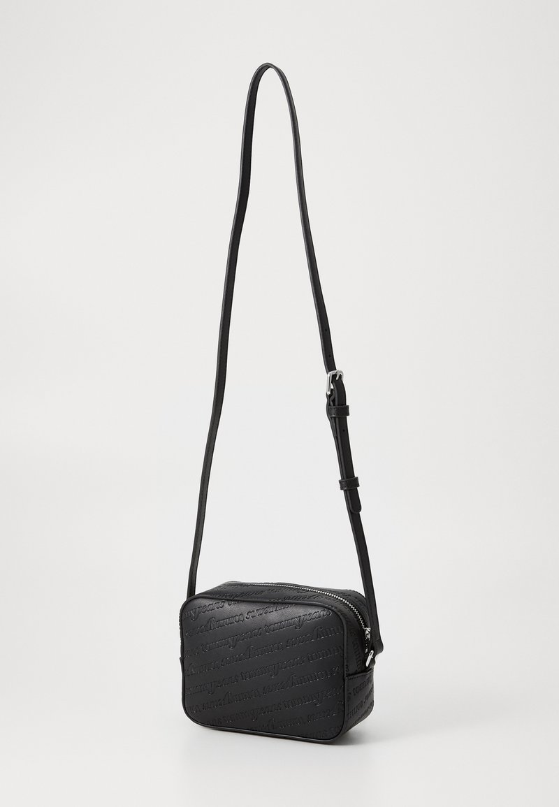 Bolso cruzado negro hecho de material texturizado, con cierre de cremallera, correa ajustable y detalle de diseño en relieve en la superficie.