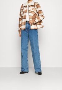 Rutig brun och cremefärgad jacka med två bröstfickor och svarta knappar, parat med högmidjade blå jeans och svarta ankelbooties.