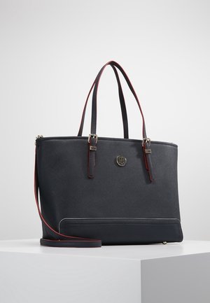 Schwarze Ledertasche mit doppelten Griffen und abnehmbarem langem Schulterriemen, versehen mit einem kleinen runden Logoemblem auf der Vorderseite.